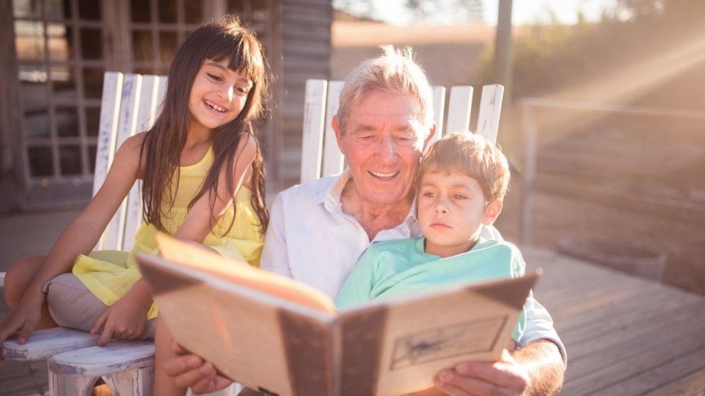 grandfather reading a book to his grandkids, smiling happy