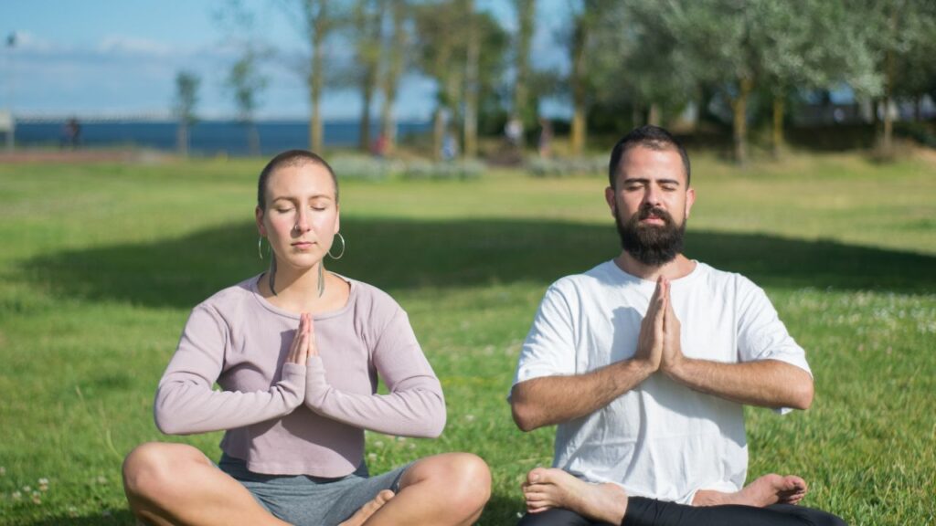 man and woman couple meditating together outside at park