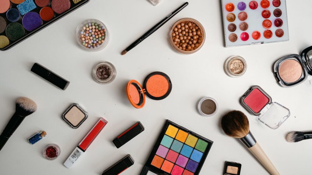 makeup items - eyeshadow, blush, lip gloss, and facial powder- spread out on a white countertop