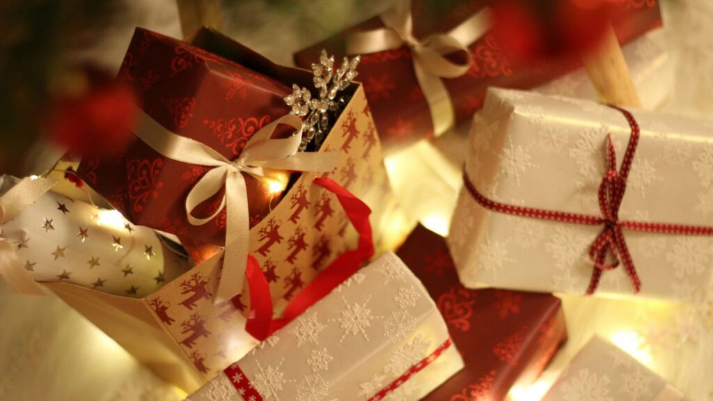 gifts wrapped in red and cream paper and ribbons beneath a Christmas tree