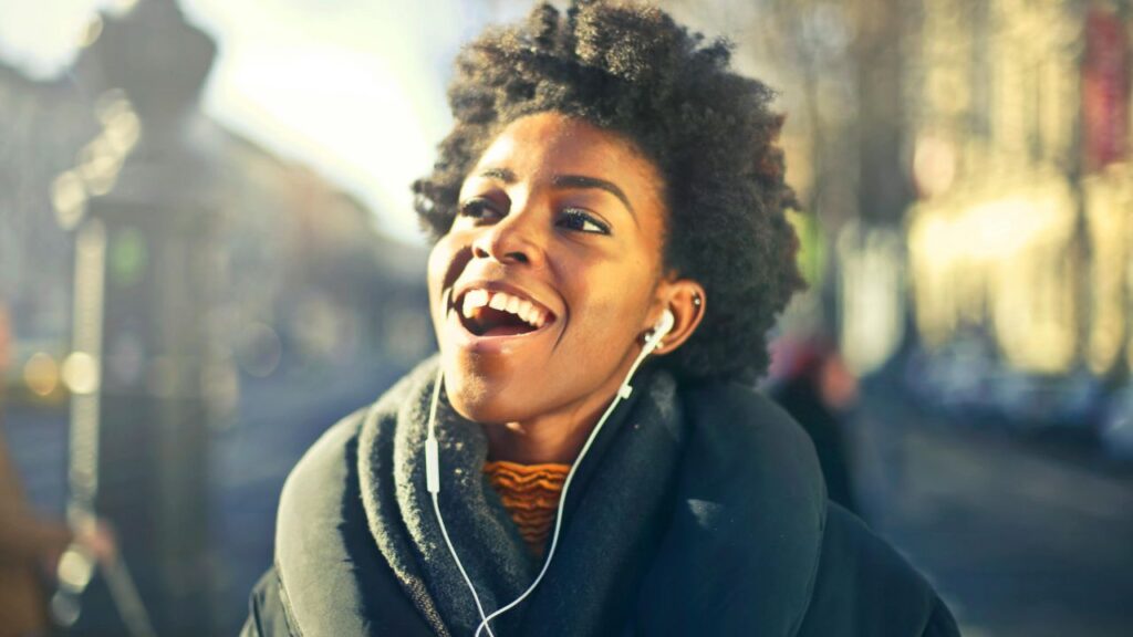 a young black woman smiling happy outside listening to music with headphones