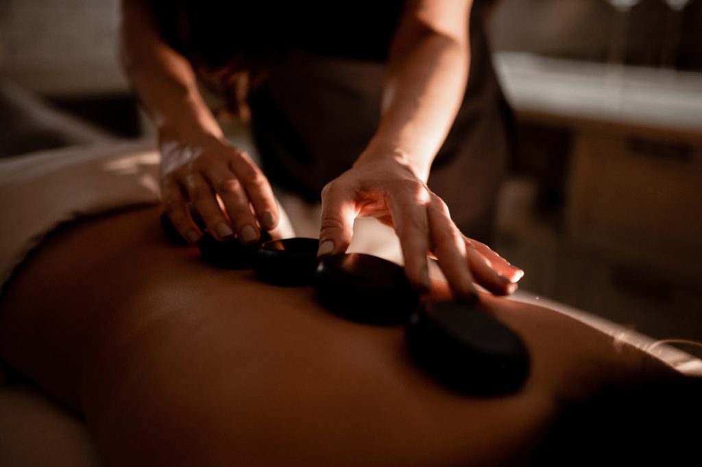 The masseuse massages the girl’s back with hot stones. Hot stone massage in the spa.